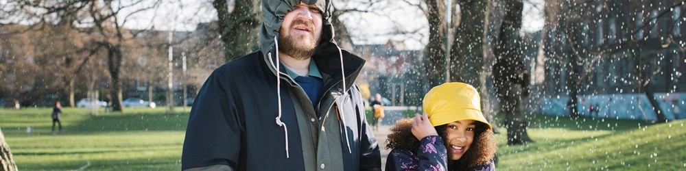 man and girl with raincoats on in park during heavy rain shower