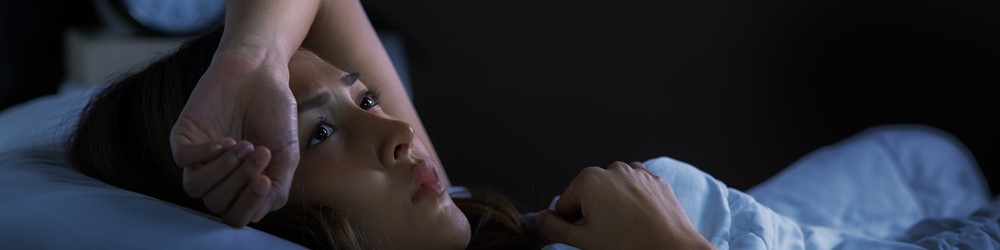 young woman awake in bed, with arm over forehead